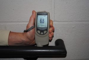 Photo 7 – Non-destructive dry film thickness gage being used to measure the thickness of the coating on hand rail. The measurement of all coats on the railing is 6.8 mils. The average of three gage readings in the same location represent a spot measurement.